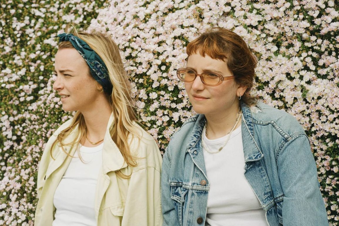 Deux femmes debout côte à côte avec des fleurs derrière elles.